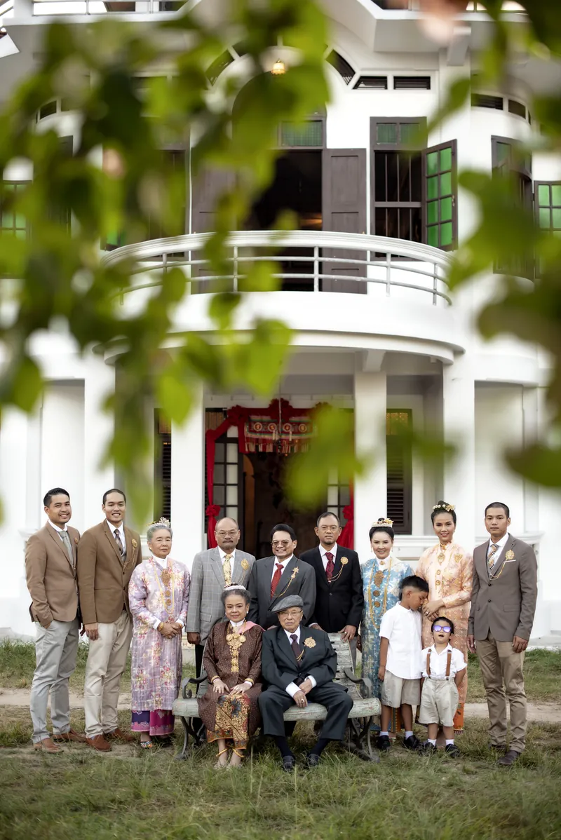 ครอบครัวสี่รุ่นในชุดบาบ๋า ถ่ายภาพหมู่หน้าบ้านอาจ้อที่ทาสีขาวเสร็จใหม่ มองผ่านใบไม้ มกราคม 2019