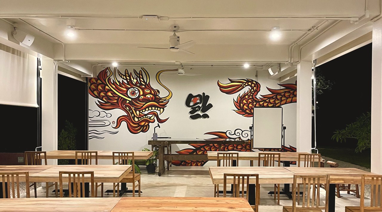 The Hok Room at Baan Ar-Jor — a fire-dragon mural on white walls above warm teak communal tables
